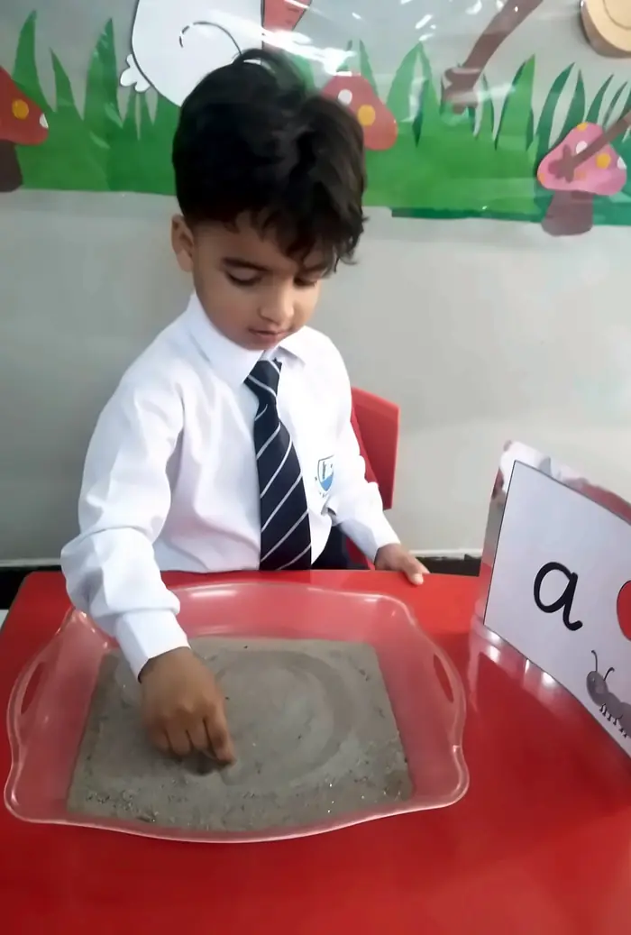 A Pre-School boy tracing a letter in the Montessori sand tray