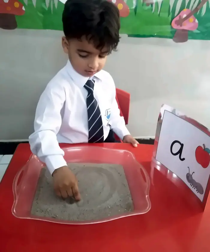 A Pre-School boy tracing a letter in the Montessori sand tray