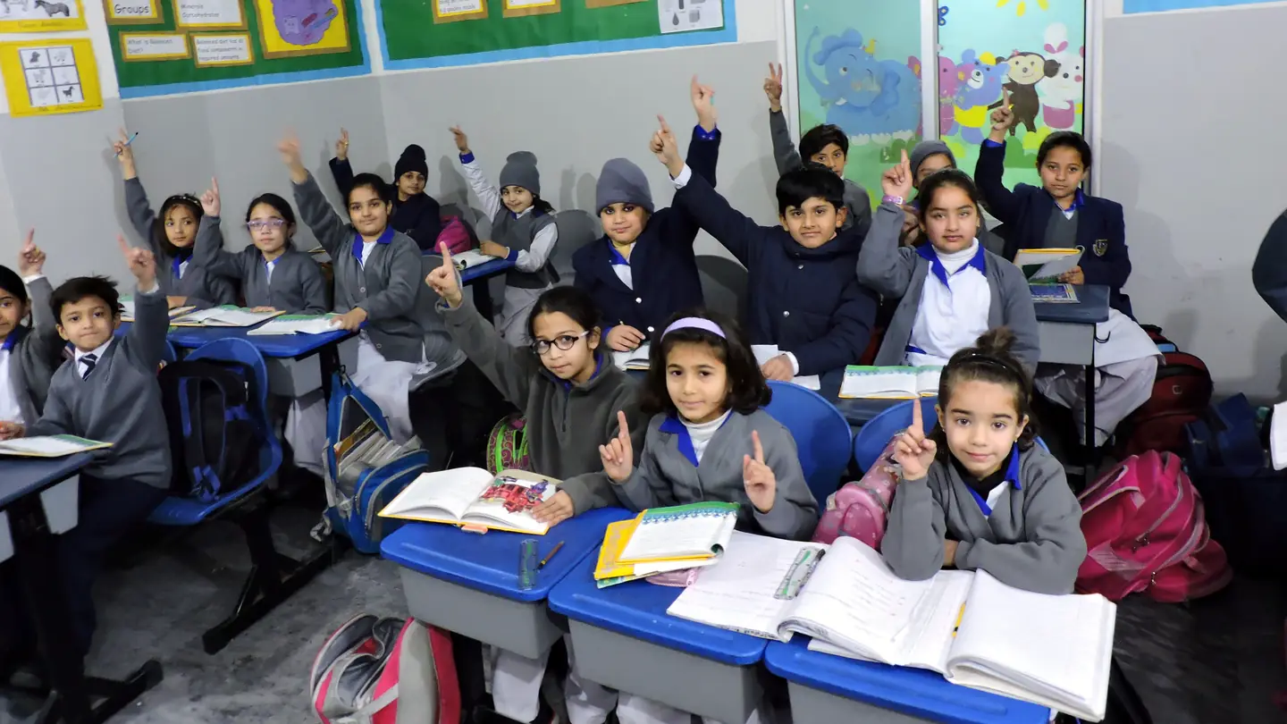 Children in a primary classroom at Lahore School System, hands raised