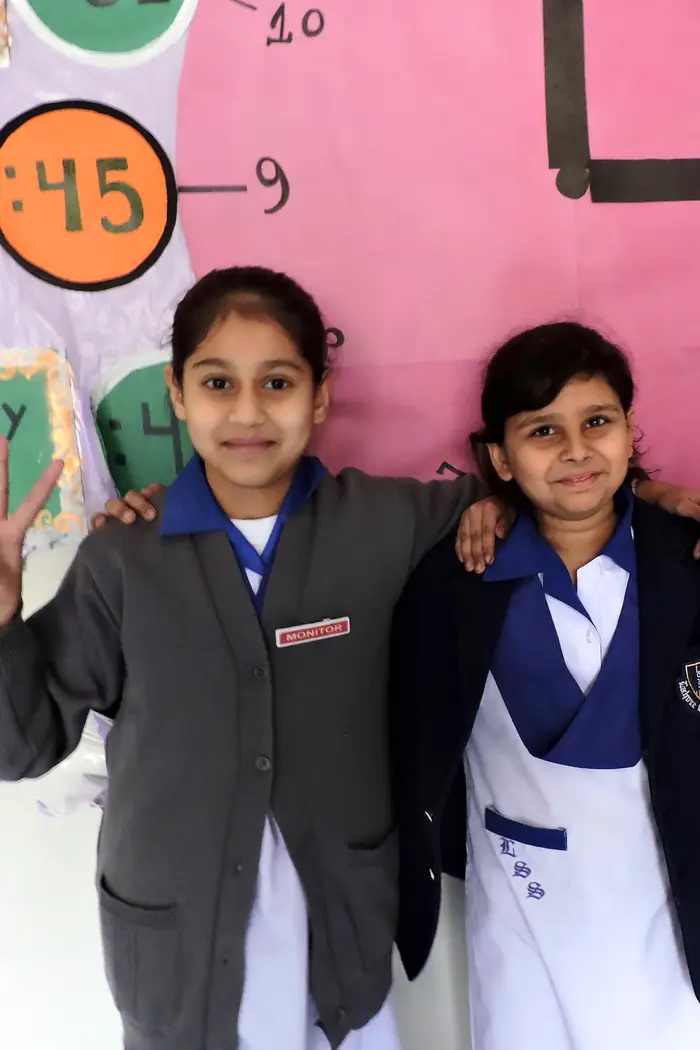 Two Primary girls by a classroom clock display